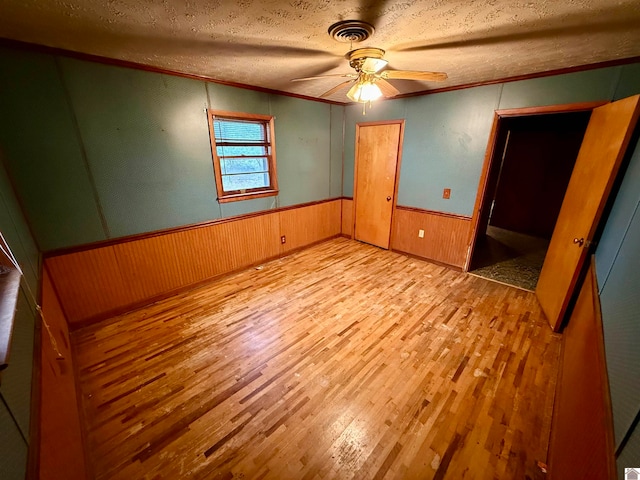 unfurnished bedroom with ceiling fan, crown molding, light hardwood / wood-style floors, a textured ceiling, and wooden walls