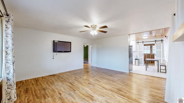 unfurnished living room with ceiling fan, a barn door, and light wood-type flooring