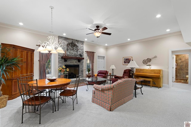 carpeted living room with ceiling fan with notable chandelier, a stone fireplace, and crown molding