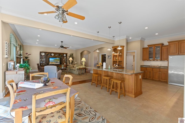 tiled dining space with ceiling fan and ornamental molding