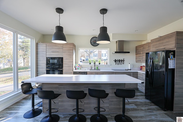 kitchen with sink, hanging light fixtures, dark wood-type flooring, wall chimney range hood, and black appliances