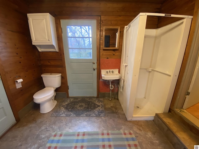 bathroom featuring a shower, sink, wooden walls, and toilet