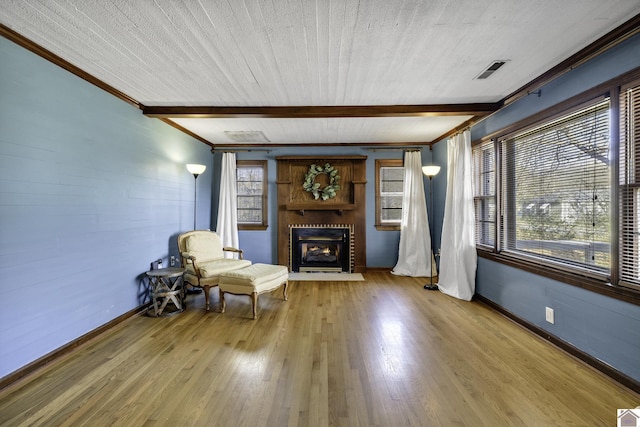 unfurnished room featuring beamed ceiling, wood-type flooring, a brick fireplace, and a healthy amount of sunlight