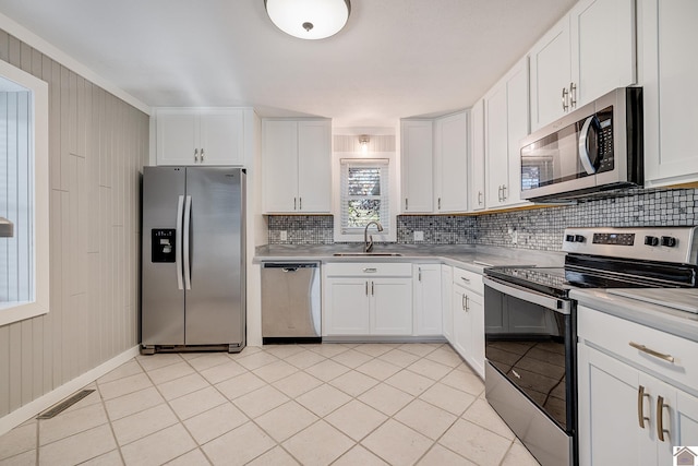 kitchen with sink, stainless steel appliances, white cabinetry, and wood walls