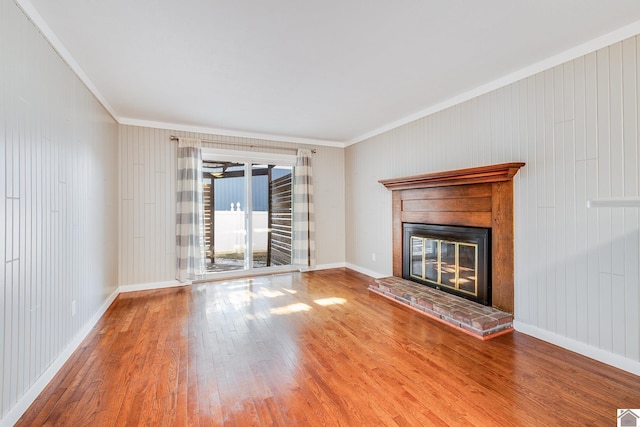 unfurnished living room featuring a fireplace, wood-type flooring, wooden walls, and ornamental molding