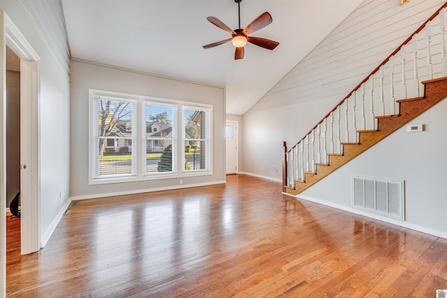 unfurnished living room featuring ceiling fan, light hardwood / wood-style flooring, high vaulted ceiling, and wooden walls