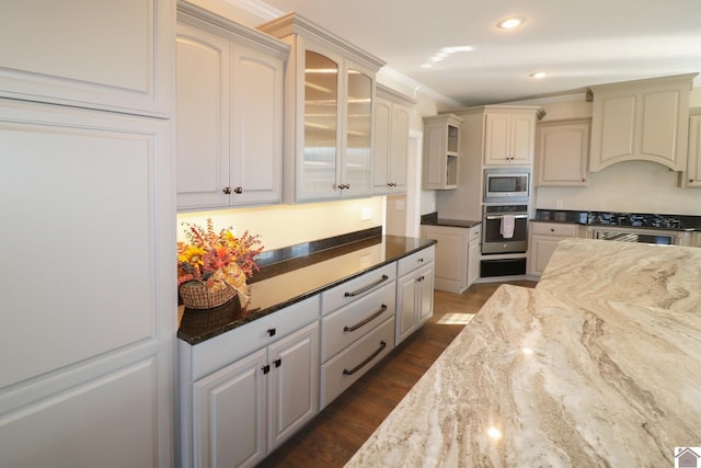 kitchen with appliances with stainless steel finishes, dark stone counters, ornamental molding, custom range hood, and dark wood-type flooring