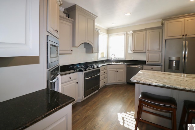 kitchen with sink, dark hardwood / wood-style floors, dark stone countertops, ornamental molding, and appliances with stainless steel finishes