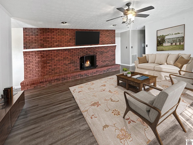 living room featuring ceiling fan, wood-type flooring, a textured ceiling, and a brick fireplace