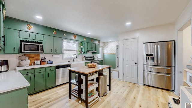 kitchen with green cabinets, light hardwood / wood-style floors, backsplash, and appliances with stainless steel finishes