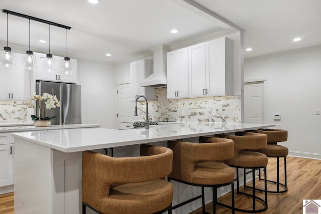 kitchen with a kitchen breakfast bar, stainless steel fridge, premium range hood, and a kitchen island with sink