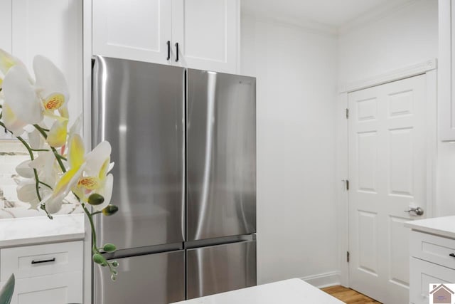 kitchen with white cabinets, light hardwood / wood-style floors, ornamental molding, and stainless steel refrigerator