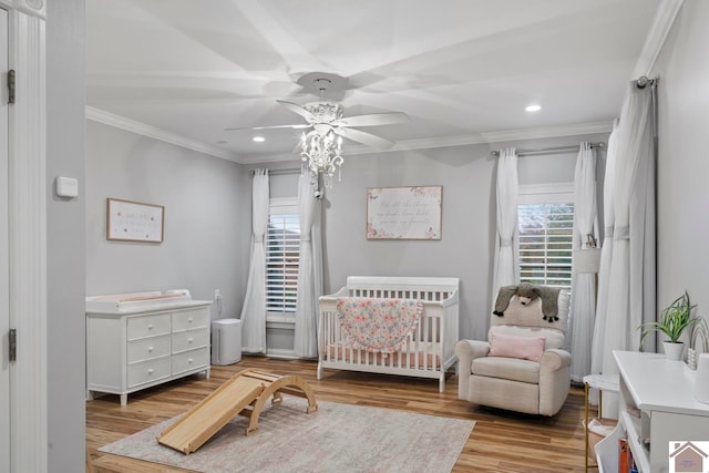 bedroom with ceiling fan, light hardwood / wood-style floors, a crib, and ornamental molding