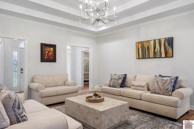 living room featuring a raised ceiling, a chandelier, dark wood-type flooring, and ornamental molding