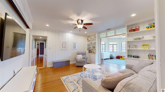 living room with light wood-type flooring, built in features, and crown molding