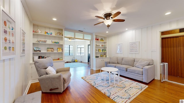 living room with built in shelves, ceiling fan, and light hardwood / wood-style flooring