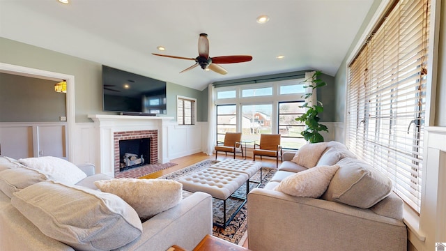 living room with ceiling fan, hardwood / wood-style floors, lofted ceiling, and a brick fireplace