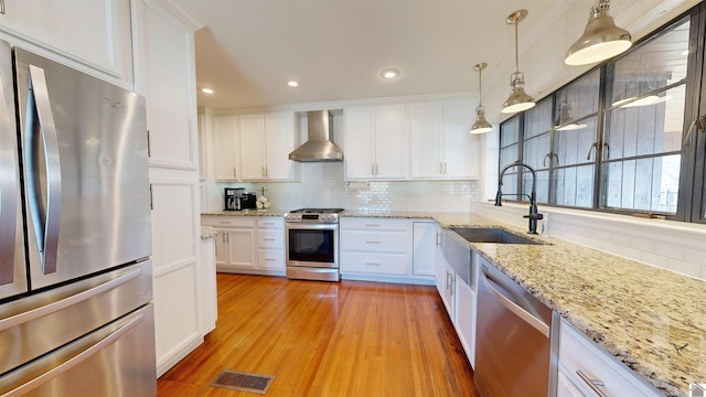 kitchen with pendant lighting, white cabinets, wall chimney exhaust hood, tasteful backsplash, and stainless steel appliances