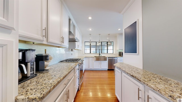 kitchen featuring hanging light fixtures, light hardwood / wood-style flooring, light stone countertops, appliances with stainless steel finishes, and white cabinetry