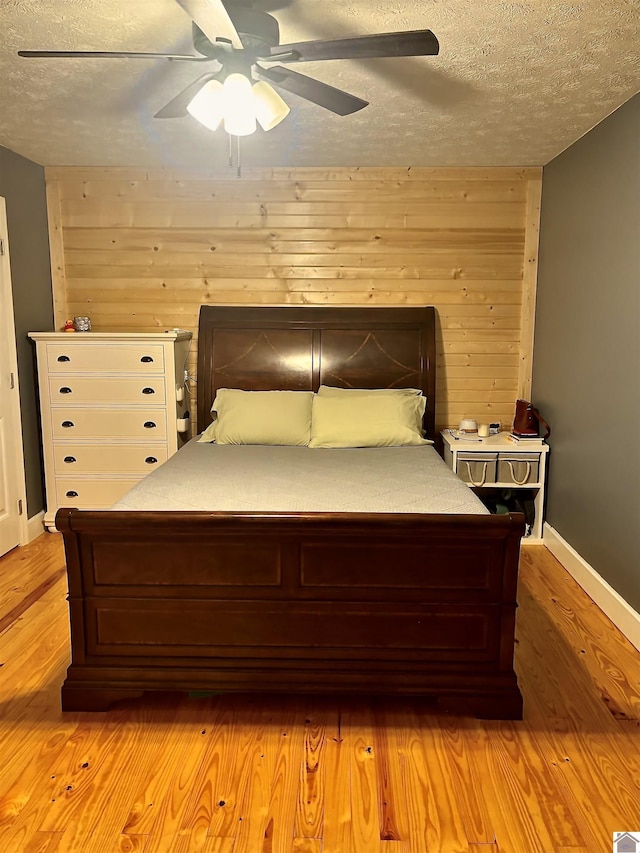 bedroom featuring ceiling fan, light hardwood / wood-style flooring, a textured ceiling, and wooden walls