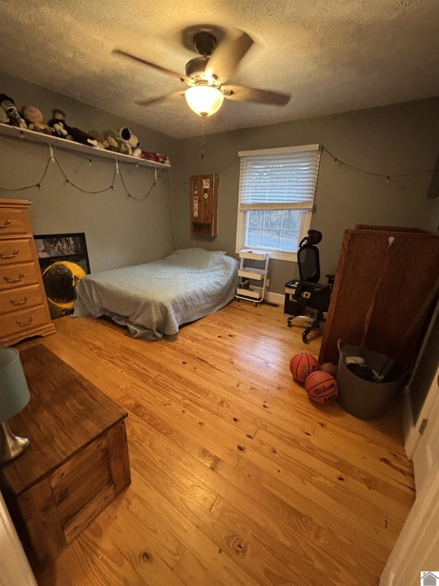 bedroom with ceiling fan, light wood-type flooring, and a textured ceiling