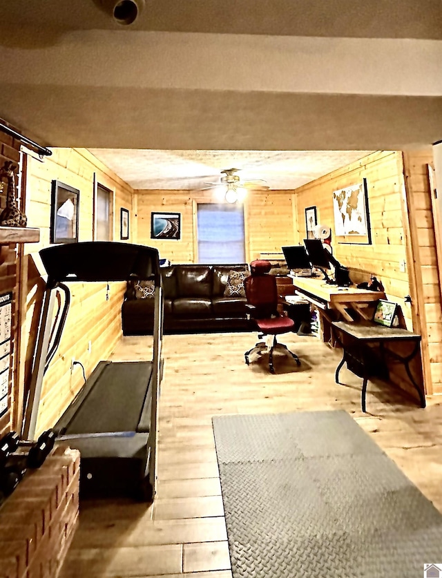 exercise room featuring wood-type flooring, ceiling fan, and wooden walls