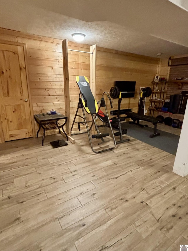 workout area featuring wood-type flooring, a textured ceiling, and wood walls