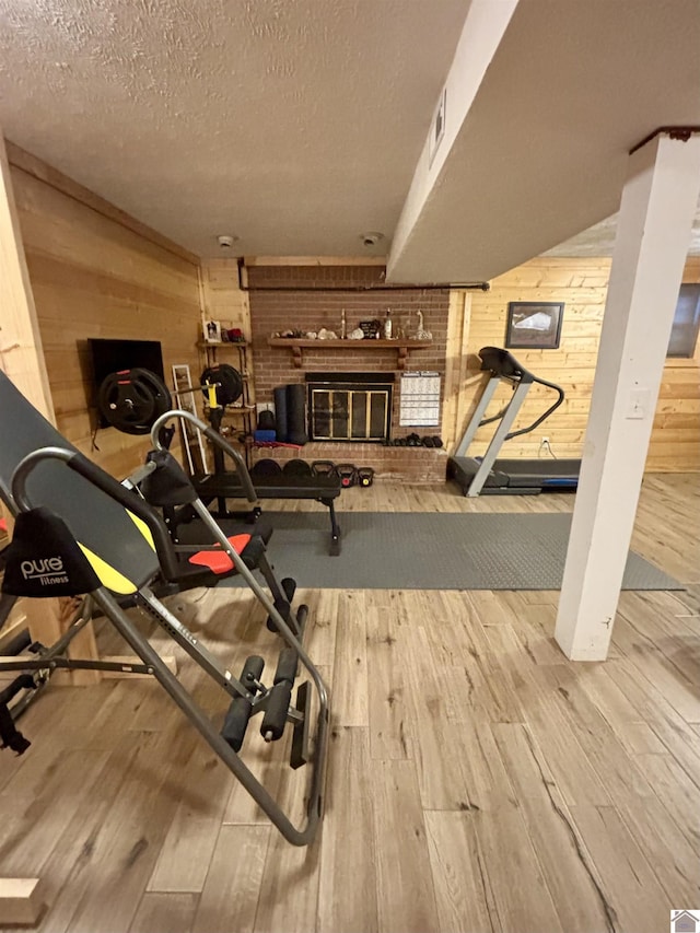 exercise room featuring a fireplace, wood walls, a textured ceiling, and light hardwood / wood-style flooring