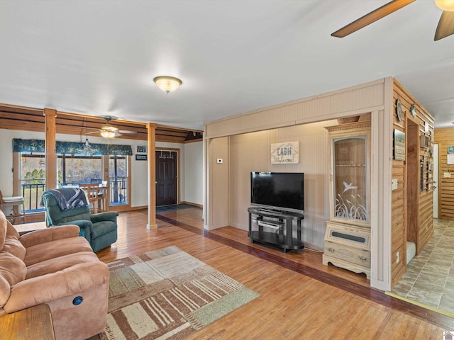 living room with ceiling fan, wood-type flooring, and wooden walls