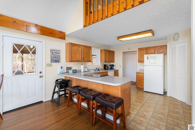 kitchen featuring a textured ceiling, light hardwood / wood-style floors, white appliances, and kitchen peninsula