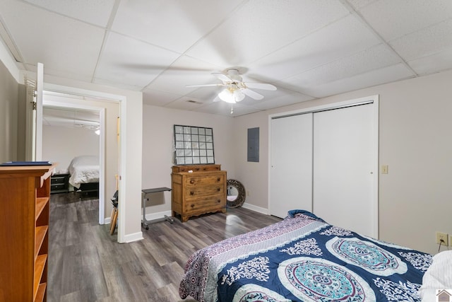 bedroom with a paneled ceiling, ceiling fan, electric panel, and wood-type flooring