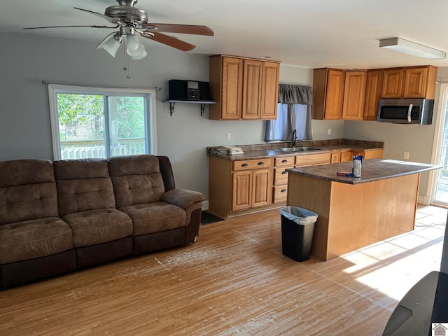 kitchen with ceiling fan, sink, a kitchen island, and light wood-type flooring