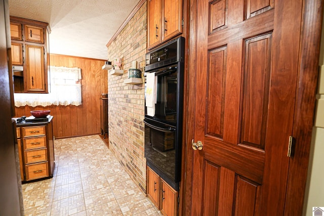 kitchen featuring brick wall, a textured ceiling, black double oven, and wood walls