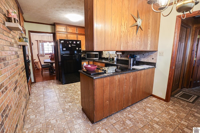 kitchen with an inviting chandelier, black refrigerator, sink, tasteful backsplash, and kitchen peninsula