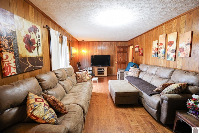 living room featuring a textured ceiling, light wood-type flooring, crown molding, and wooden walls