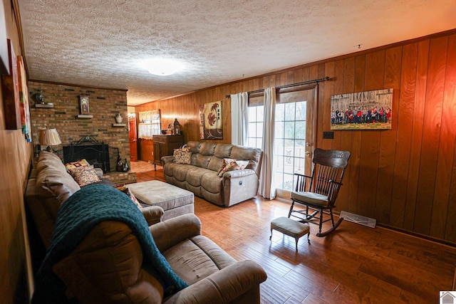 living room with a fireplace, wood-type flooring, a textured ceiling, and wooden walls