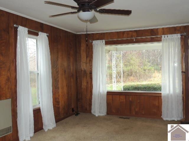 unfurnished room with light carpet, crown molding, ceiling fan, and wooden walls