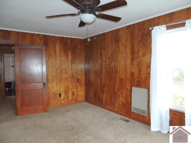 carpeted empty room featuring ceiling fan, wood walls, and ornamental molding