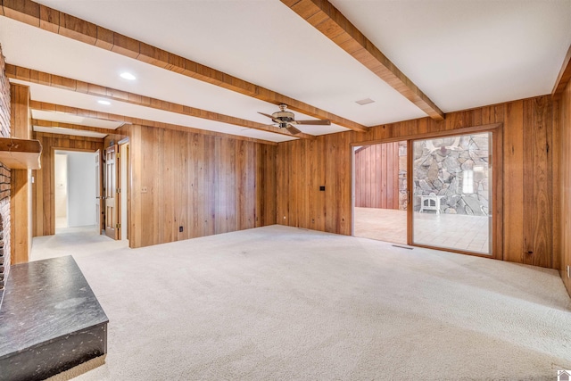 unfurnished living room with beam ceiling, ceiling fan, a large fireplace, wood walls, and carpet