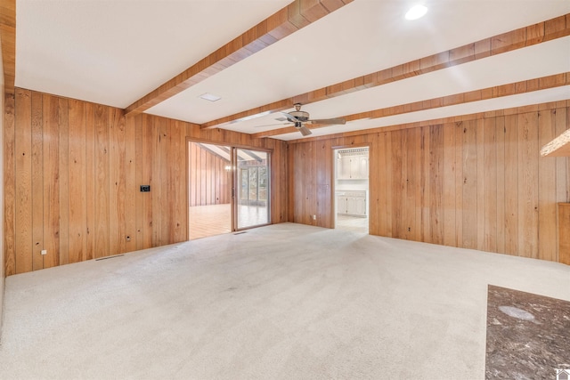 carpeted empty room with beamed ceiling, ceiling fan, and wooden walls