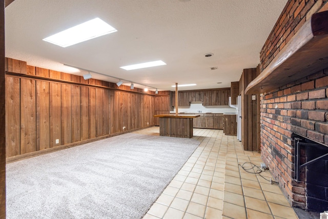 basement with a textured ceiling, wood walls, light tile patterned flooring, and track lighting