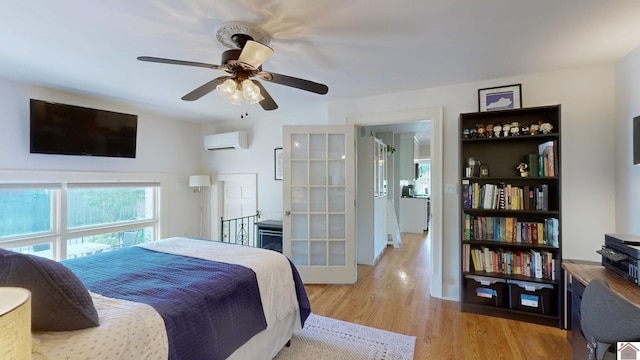 bedroom featuring ceiling fan, light hardwood / wood-style floors, an AC wall unit, and french doors