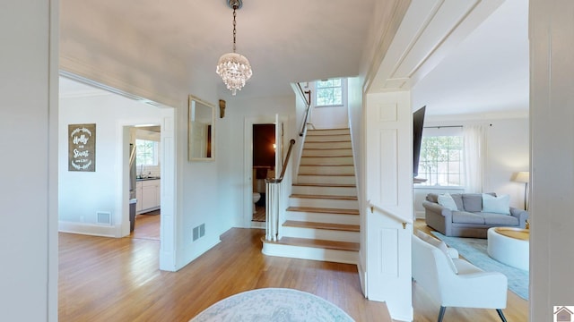 staircase with wood-type flooring, an inviting chandelier, and crown molding