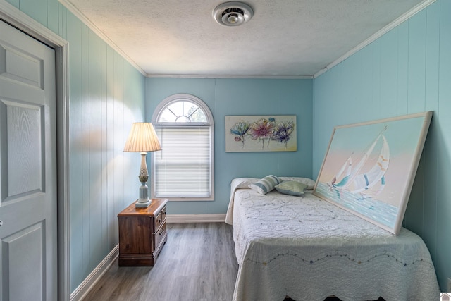 bedroom featuring wood walls, ornamental molding, a textured ceiling, and hardwood / wood-style flooring