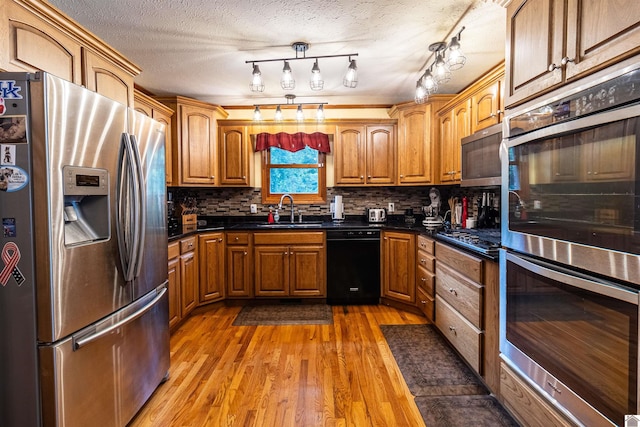 kitchen with decorative backsplash, appliances with stainless steel finishes, a textured ceiling, sink, and hardwood / wood-style floors