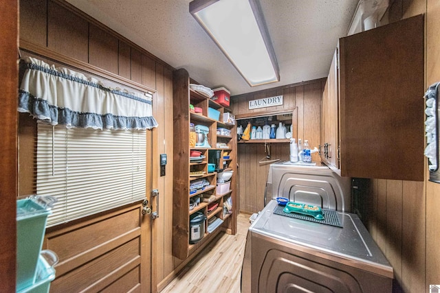 laundry room featuring wooden walls, cabinets, a textured ceiling, and light wood-type flooring