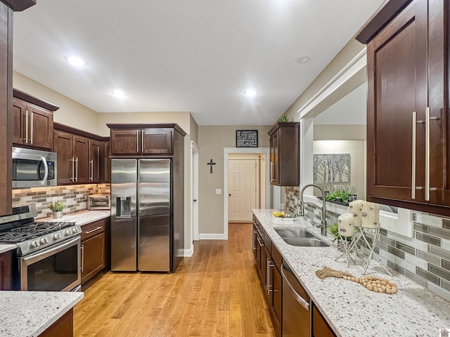 kitchen with sink, light hardwood / wood-style flooring, appliances with stainless steel finishes, tasteful backsplash, and light stone counters