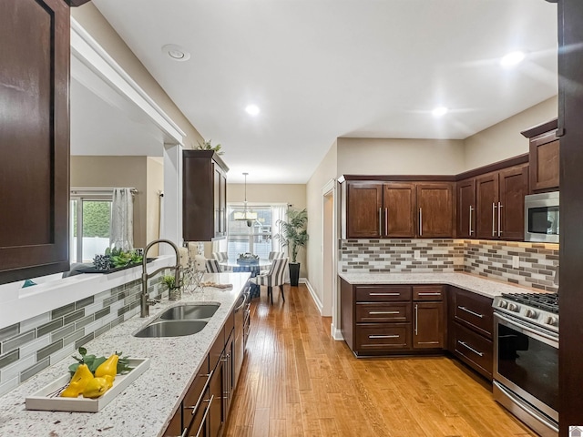 kitchen featuring tasteful backsplash, stainless steel appliances, sink, decorative light fixtures, and light hardwood / wood-style flooring