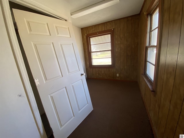 hall with dark colored carpet and wooden walls