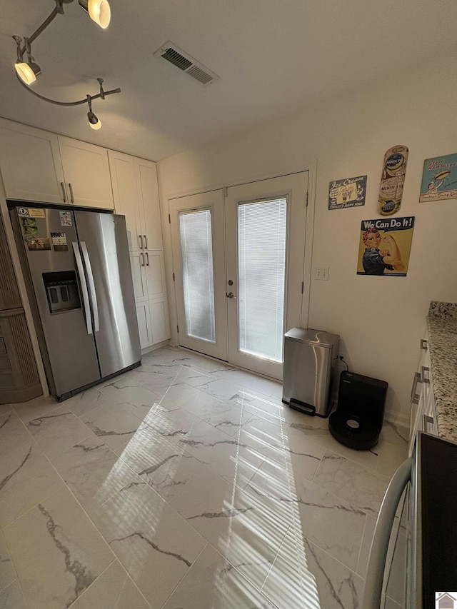 kitchen featuring stainless steel refrigerator with ice dispenser, rail lighting, french doors, light stone counters, and white cabinetry